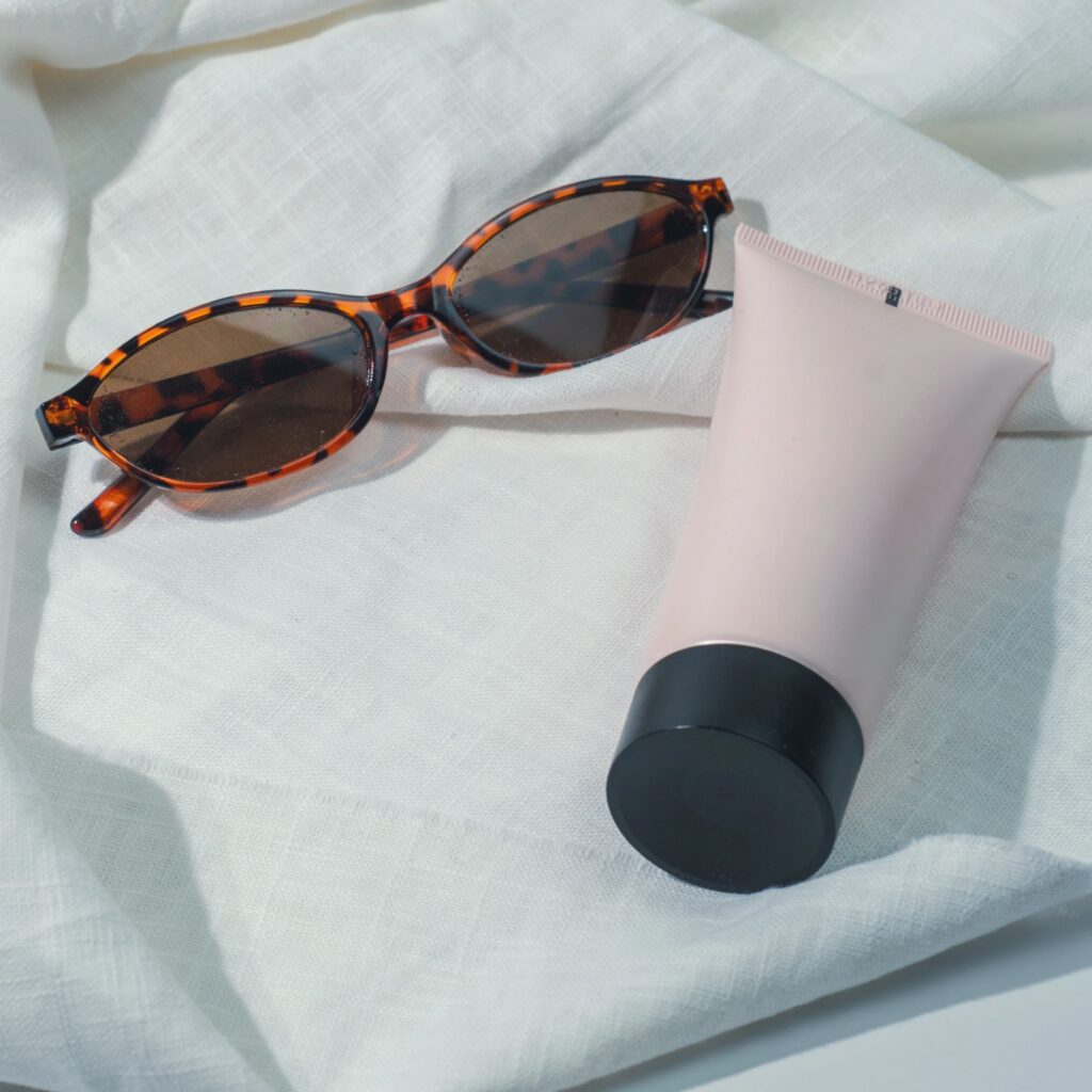 Close-up of sunglasses and pink sunscreen tube on white linen